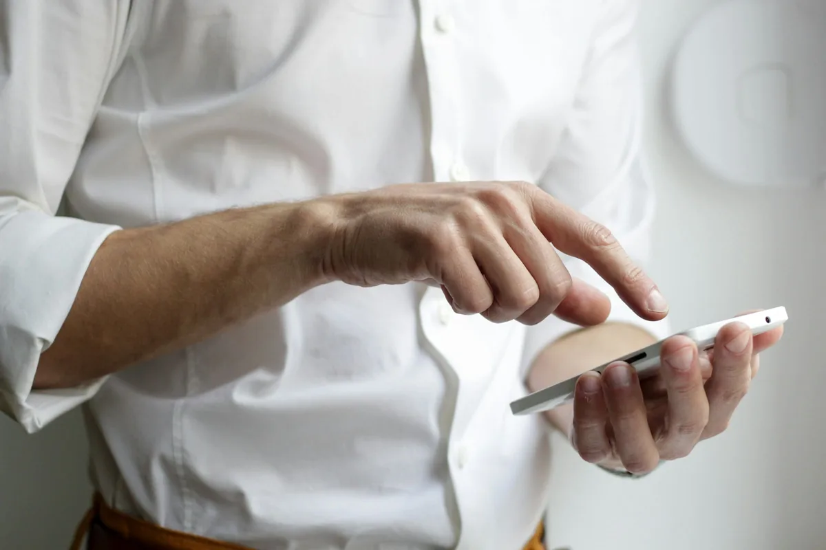 Persona con camisa blanca consultando un teléfono móvil, en el momento de pedir una cita de servicio técnico