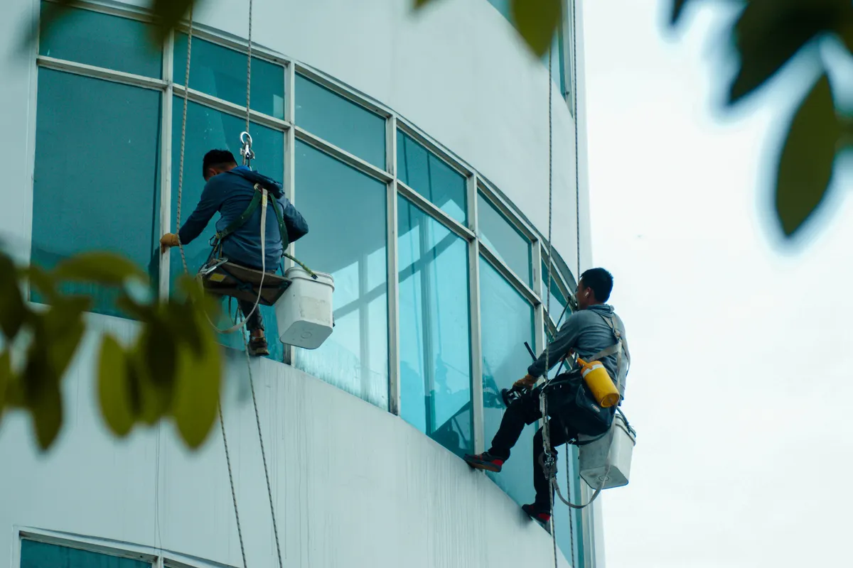 Limpiacristales suspendidos con cuerdas limpiando la fachada de cristal de un edificio alto