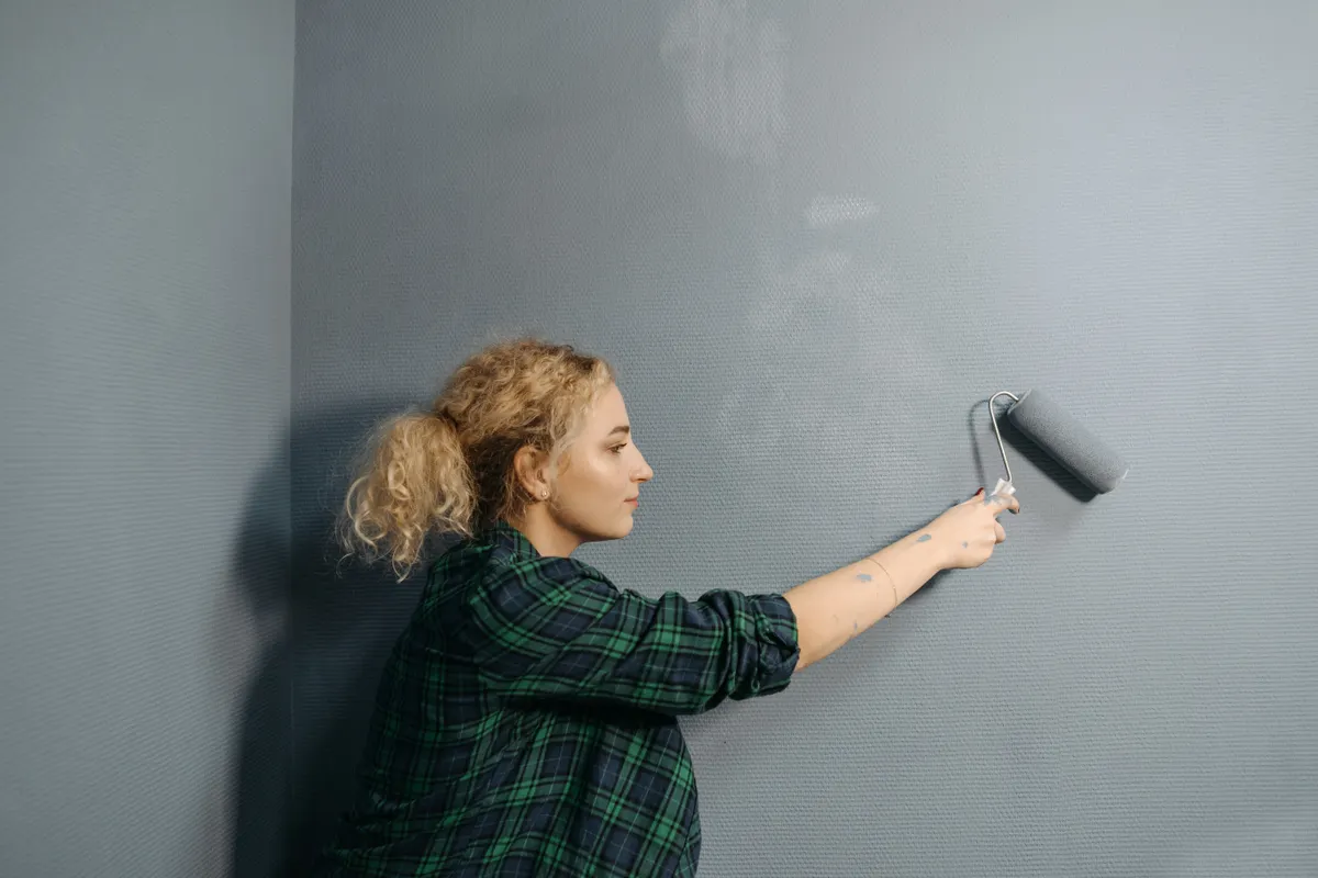Mujer joven aplicando pintura gris con un rodillo en una pared interior
